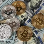 A mix of gold and silver Bitcoin tokens placed on top of US hundred-dollar bills