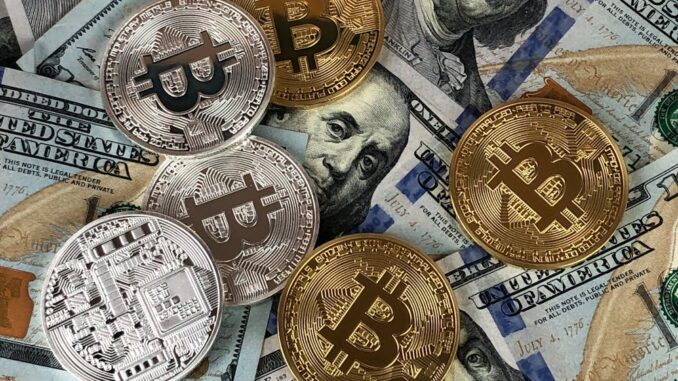 A mix of gold and silver Bitcoin tokens placed on top of US hundred-dollar bills