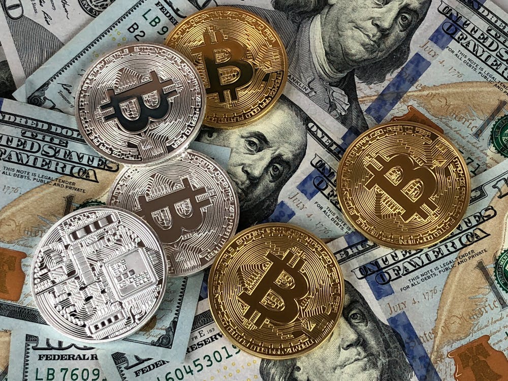 A mix of gold and silver Bitcoin tokens placed on top of US hundred-dollar bills